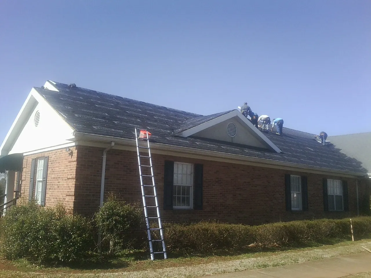 Crew tearing shingles off a brick ranch roof with a ladder set — Emergency Roof Repair work by our crew in Columbia Cross Roads
