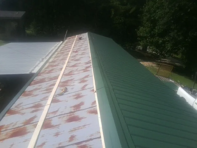 Old rusted panels beside newly installed green metal roofing — Wind Damage Roof Repair by Roofing Brothers in Columbia Cross Roads