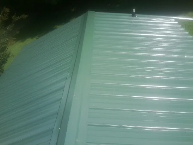 New green metal panels meeting at the ridge of a roof — Flat Roof Repair work by our crew in Columbia Cross Roads