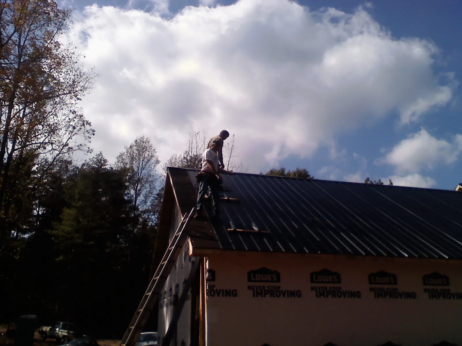 Roofer fastening dark metal panels high against a cloudy sky, from a Roof Inspection job in Columbia Cross Roads