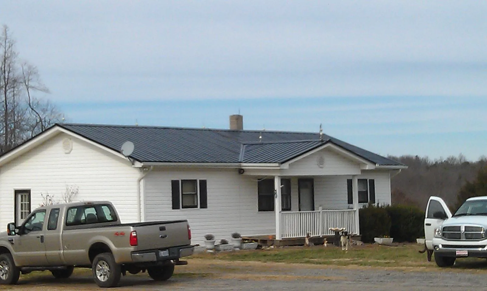 Finished dark metal roof on a white ranch home with work trucks parked in Columbia Cross Roads
