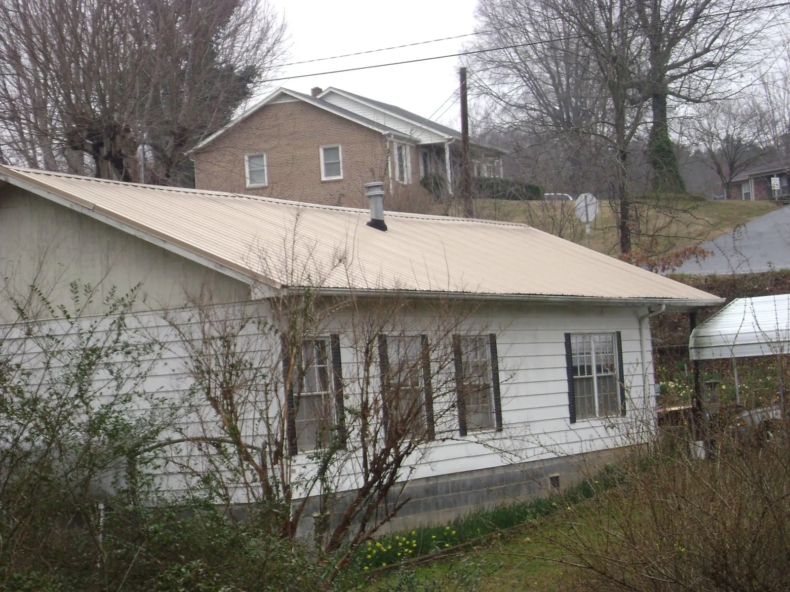 Tan metal roof on a white sided house set into a hillside — Commercial Roofing by Roofing Brothers in Columbia Cross Roads
